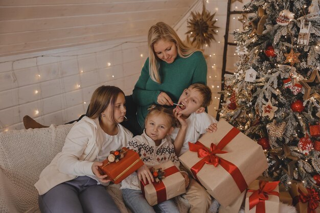 Morher and Kids in new year's Christmas atmosphere. Family are happy with Christmas and gifts. Children at the New Year tree with gifts.