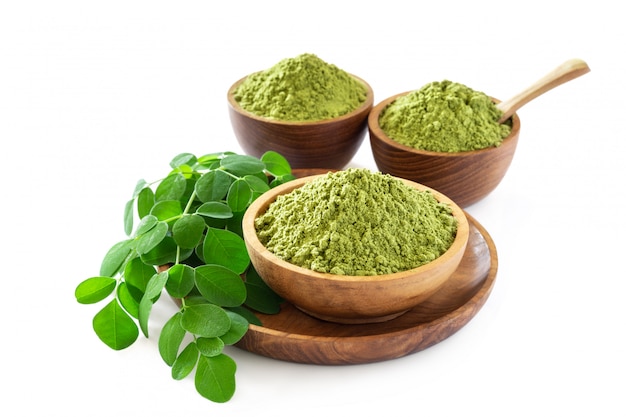 Moringa powder in wooden bowl with original fresh Moringa leaves isolated on white background.