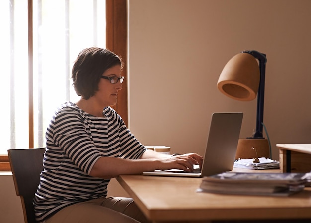 Photo morning admin a cropped shot of a woman sitting at a desk in her home and working on a laptop