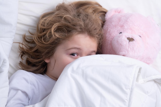 Morning awakening little child with toy teddy bear in bed kid wakes up in the bedroom