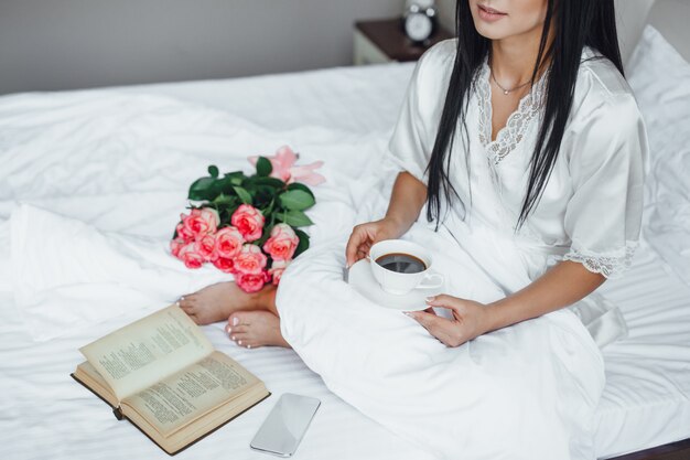 Mattina di una bella ragazza con libro e rose