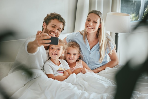 Morning bed and happy family take a selfie with a smile enjoying quality time bonding and relaxing at home Pictures mother and father with young children kids or siblings in the house bedroom