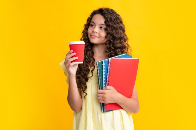 Morning before school Student teen girl with books hold takeaway delivery cup coffee isolated on yellow background Education in college concept Smiling schoolgirl