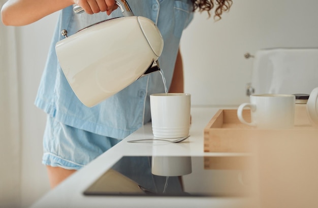 Утренний кофе для завтрака и женские руки наливают воду в чашку из ретро-чайника на кухне дома Женщина в пижаме заваривает чай или готовит напиток на прилавке, чтобы начать день
