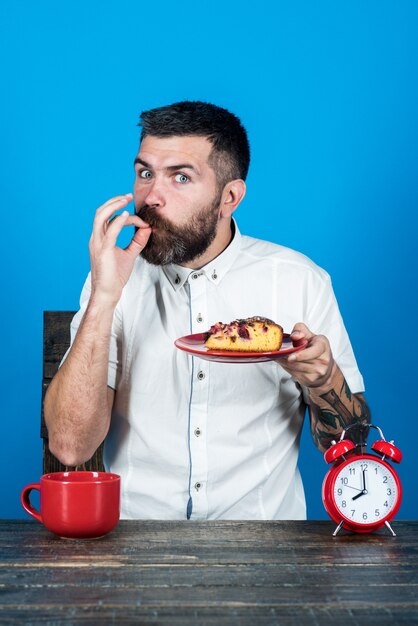 Morning breakfast fooddrink gesture concept handsome bearded man hold plate with tasty pie shows