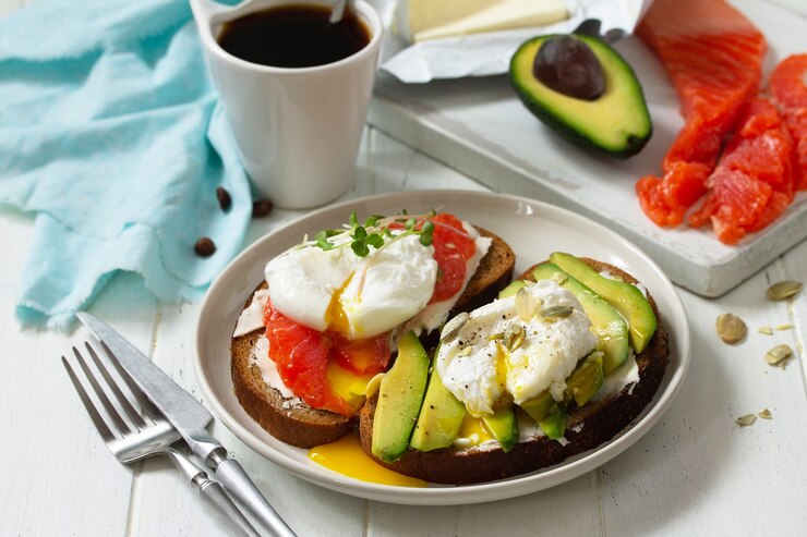 朝の朝食ポーチドエッグゆでサンドイッチ、アボカドサーモンとコーヒーと木製のテーブル
