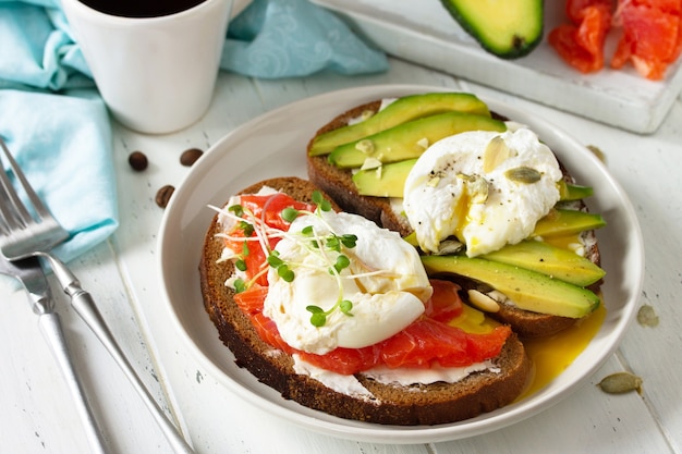 Colazione mattutina panino bollito con uova in camicia con salmone avocado e caffè su un tavolo di legno