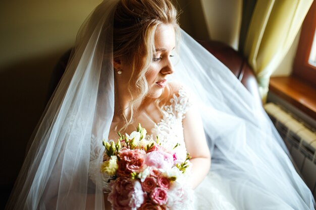 Morning of the bride. Beautiful bride in white wedding dress with bridal bouquet at wedding morning.