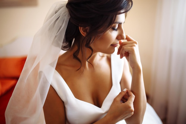 Утром невесты красивая улыбающаяся брюнетка в белом платье с свадебным букетом в руках
