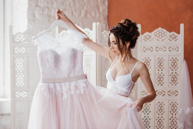 Morning bride with bridesmaid. She holds a beautiful pink wedding dress in her hands. Collect. Prepare for the wedding.