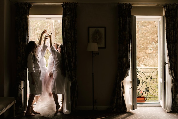 Morning of the bride with girlfriends with glasses in their hands near the window