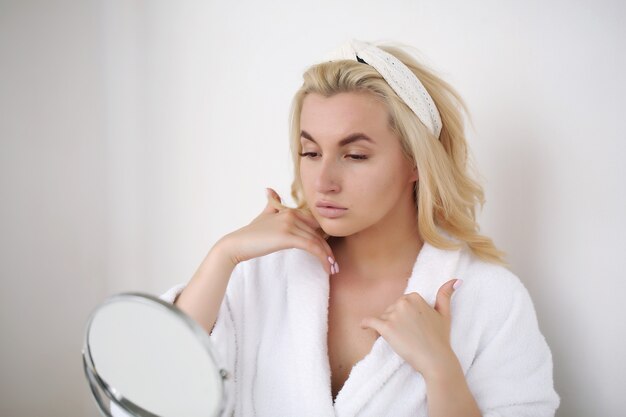 Morning care, a young girl in a bathrobe and with a white towel uses body cream.