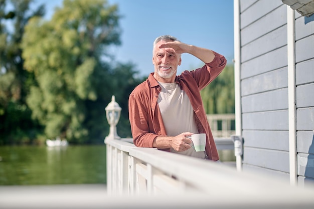 Morning coffee. Confident bearded gray-haired man with a cup in hands