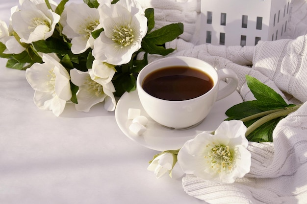 Morning coffee in a white cup, white anemone flowers nearby. Free space for text.