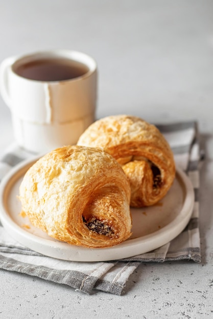 Morning concept Two fresh croissants on a white plate on a napkin with tea on light background