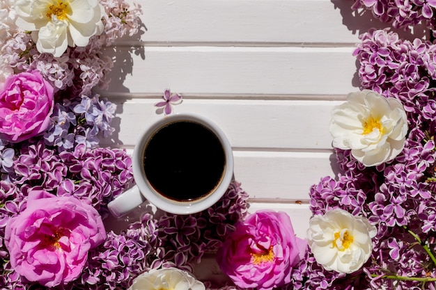 Morning cup of black coffee and branch of blooming purple lilac with green leaves on white background.composition with white cup of coffee,beautiful bouquet of lilacs. concept of spring and comfort.