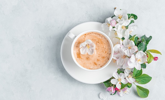 A morning cup of coffee and flowers on a light gray wall. Top view, copy space.