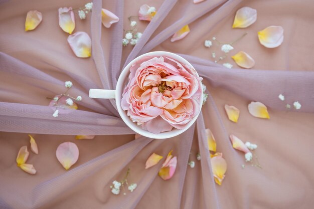 Photo morning cup of coffee with beautiful rose flowers on pink fabric delicate pastel floral background top view gentle breakfast in womens valentines or wedding day flat lay luxury wedding concept