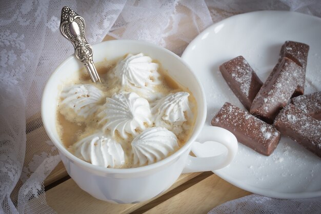 Утренняя чашка горячего кофе с зефиром и шоколадом. Вкусный завтрак.