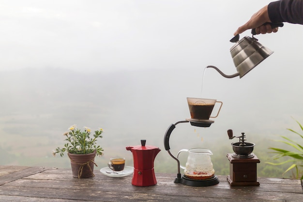 木製のテーブルにロータリーコーヒーグラインダーとフラワーポットとコーヒーの朝のカップ