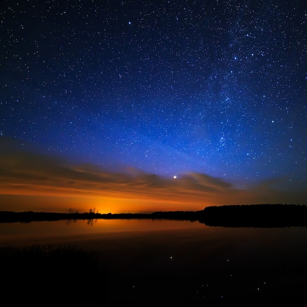 Morning dawn on a starry background sky reflected in the water of the lake.