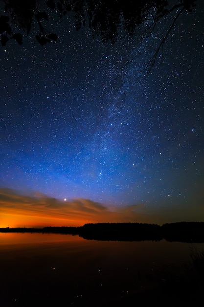 Утренний рассвет на звездном фоне неба отражается в воде озера.