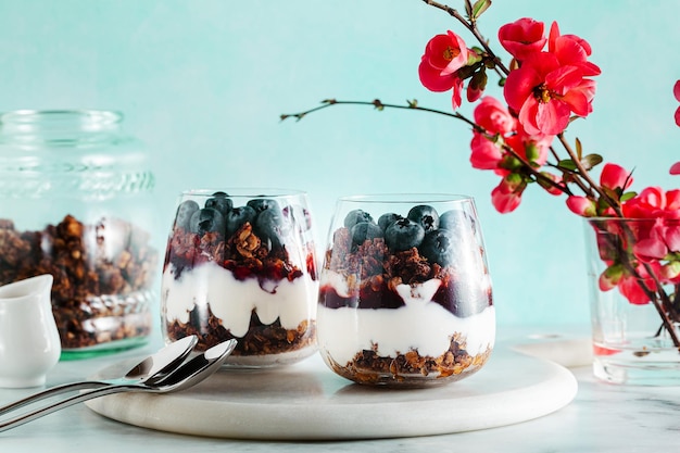 Фото Утренний десерт с мюсли в стакане с йогуртовым джемом и свежими ягодами весенние ветки цветущего дерева здоровый завтрак