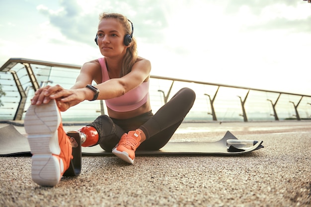 Photo morning exercises young beautiful woman in headphones with leg prosthesis listening music and