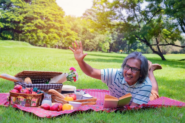 Al mattino sta leggendo un libro, sorride e ride. è sdraiato sull'erba accanto al picnic