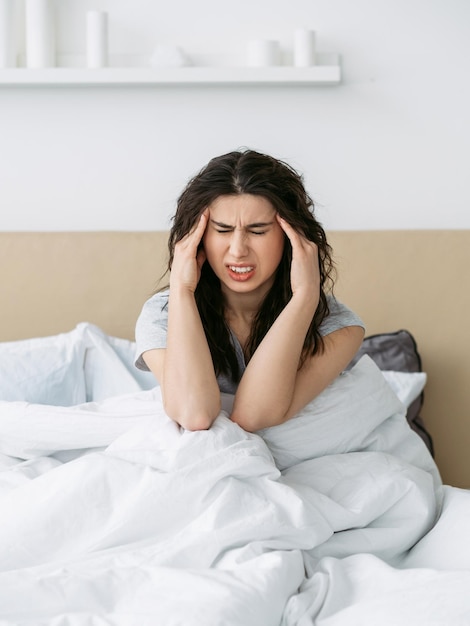 아침 두통 불면증 문제 수면 장애 아픈 고통받는 여성이 밝은 침실에서 혼자 흰색 침대에 앉아 사원을 마사지