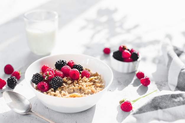 Morning healthy breakfast, white bowl full with granola, muesli, raspberry, blackberry on gray concrete table. Healthy eating, eco, bio food concept. Fresh tasty meal on grey background. Quality photo