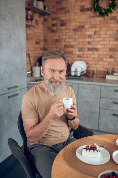 Morning at home. A bearded amn sitting at the table in the kitchen and looking contented