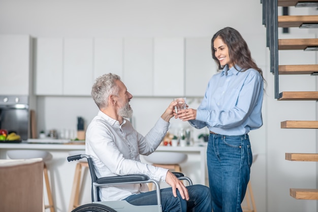 Morning at home. Gray-haired handicapped man and his young wife in the kitchen getting the breakfast ready