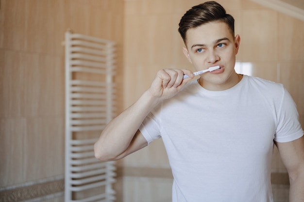 Foto l'igiene del mattino, il ragazzo si lava i denti vicino allo specchio