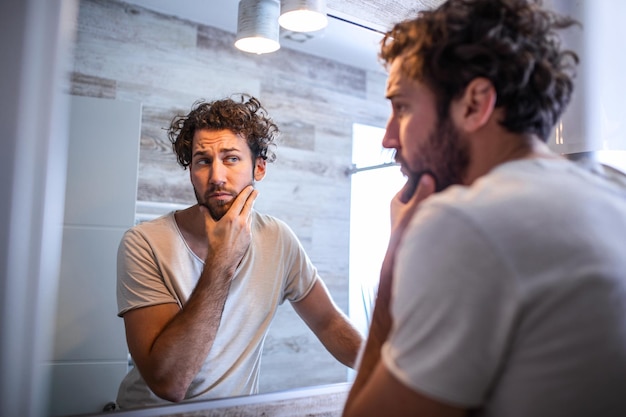 Morning hygiene, Handsome man in the bathroom looking in mirror. Reflection of handsome man with beard looking at mirror and touching face in bathroom grooming