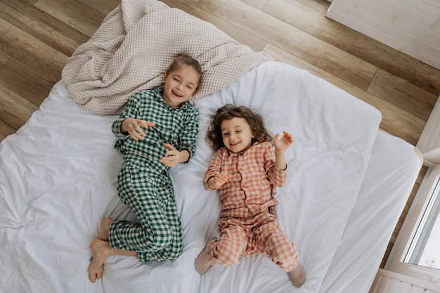 Photo morning kids top view happy sisters are lying in a bed morning awakening little girls in a bed