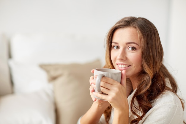 Photo morning, leisure, christmas, winter and people concept - happy young woman with cup of coffee or tea at home