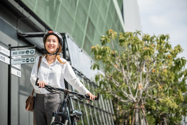 Photo morning motion and happiness an asian businesswoman in a helmet and suit stands with her bicycle this image portrays the concept of a joyful business commuter harmonizing work and outdoor activity