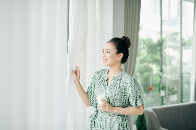 Morning portrait of young smiling woman drinking milk from the glass