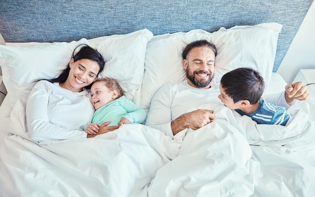 Photo morning relax and happy with family in bedroom for wakeup affectionate and bonding from top view smile care and sleeping with parents and children in bed at home for playful happiness or support