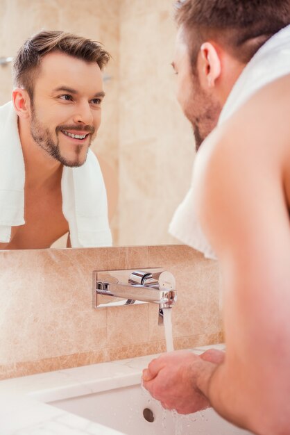 Foto la routine del mattino. bel giovane lavarsi le mani in bagno mentre si trova davanti allo specchio