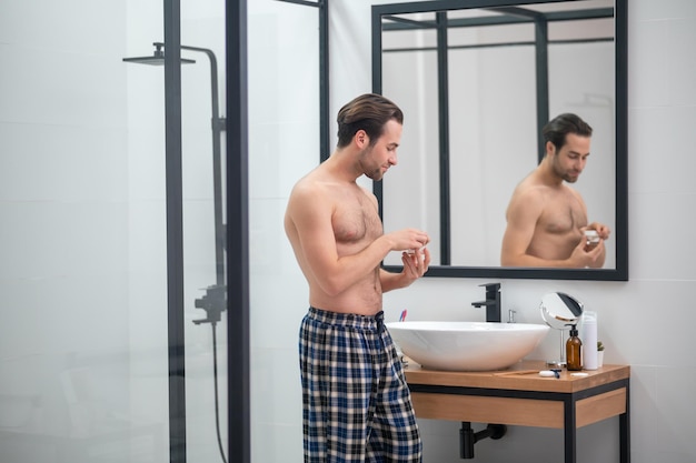 Morning routine. Man in plaid home pants standing at the mirror