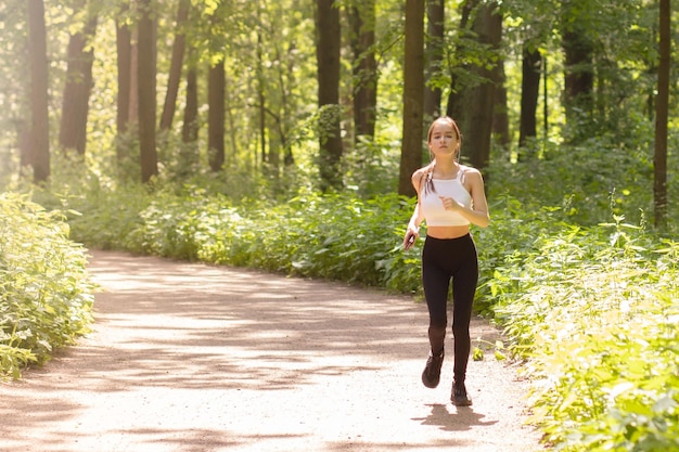 公園での朝のランニングヘッドフォンを着た少女がスポーツに出かける