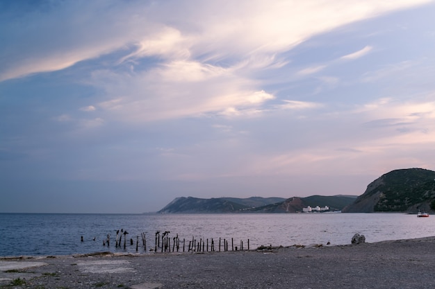 Morning on the sea with beautiful white clouds, mountainous coastline and stony shore.