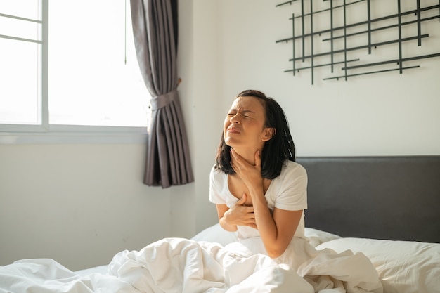 Morning sickness. Young pregnant woman sitting on bed, covering her mouth feeling nauseous during pregnancy, Woman in white pajamas suffering from Acid reflux while wake up on her bed in the morning.