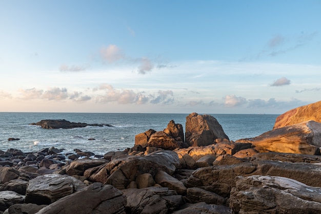 In the morning, the sun shines on the rocks and waves on the beach;