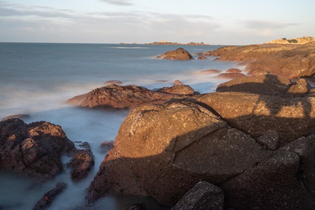 In the morning, the sun shines on the rocks and waves on the beach;