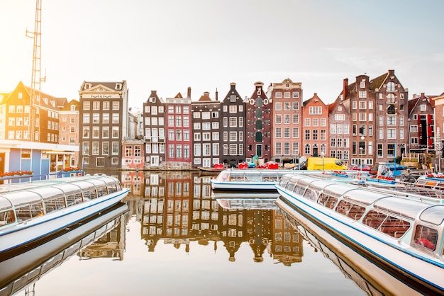 Morning view on the beautiful buildings and boats on the Damrak avenue in Amsterdam