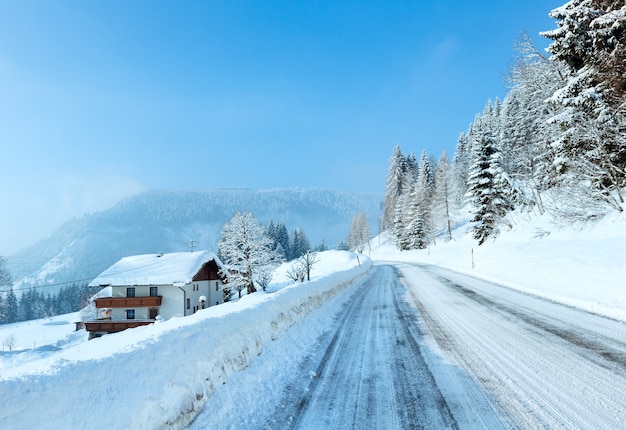 Утренняя зима туманный сельский вид с альпийской дорогой и домом на обочине дороги.