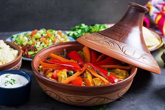 Moroccan food. Traditional tajine dishes, couscous  and fresh salad  on rustic wooden table. Tagine chicken meat and vegetables. Arabian cuisine.